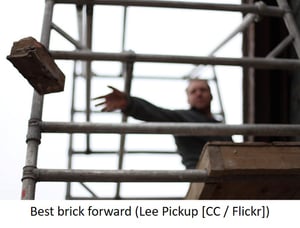 Bricklayer throwing brick from scaffolding.