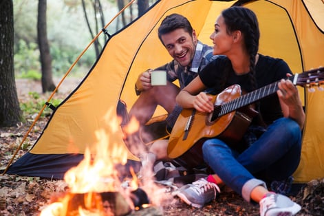 Portrait of a young couple sitting with guitar near bonfire in the forest