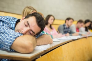 Male sleeping with students sitting in the college lecture hall