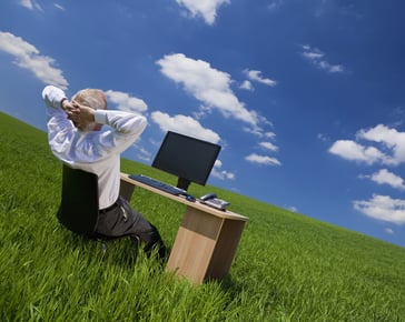 Man sitting at his desk in a field admiring a blue sky